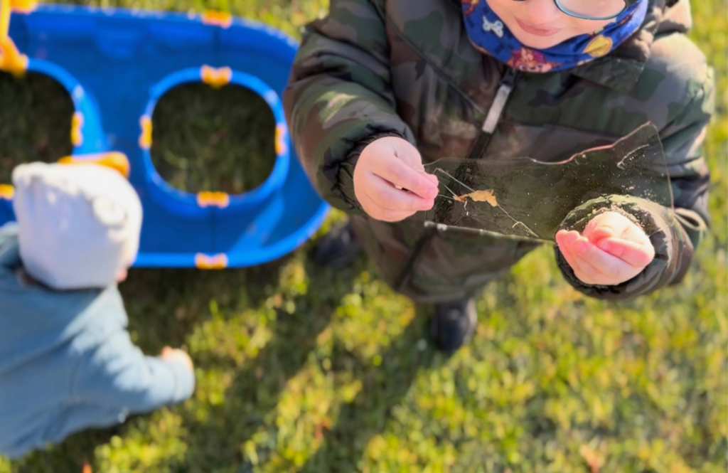 Boy is holding a transparent ice slate which has a frozen leaf inside. 